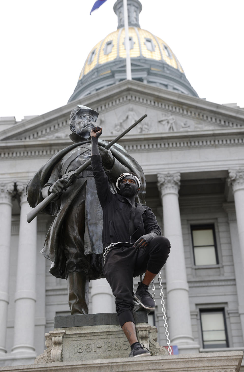 FILE - In this June 6, 2020 file photo, a demonstrator raises his fist after chaining himself to the Civil War Monument during protests over the death of George Floyd in front of the State Capitol in downtown Denver. On Thursday, Feb. 25, 2021, state lawmakers are considering what to put on the pedestal on which the monument stood until it was toppled in late June 2020. (AP Photo/David Zalubowski, File)