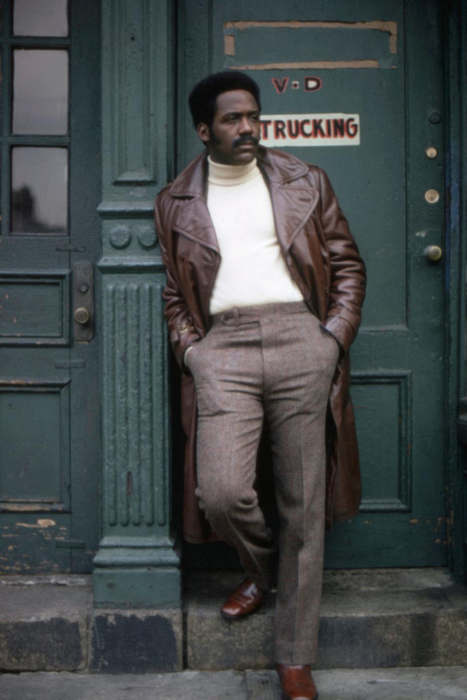 Richard Roundtree in a brown lether jacker leaning against a building