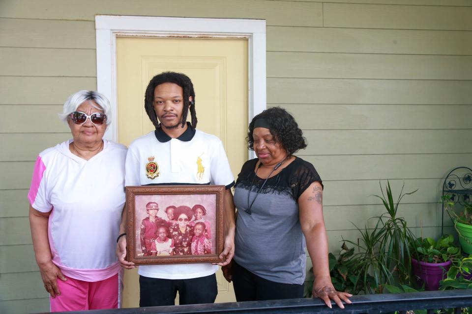 Shirly Francis stands with her grandson Akeem Davis, and daughter Felicia Shiggs as Davis holds a family photo showing his father, William Harvey as a boy.