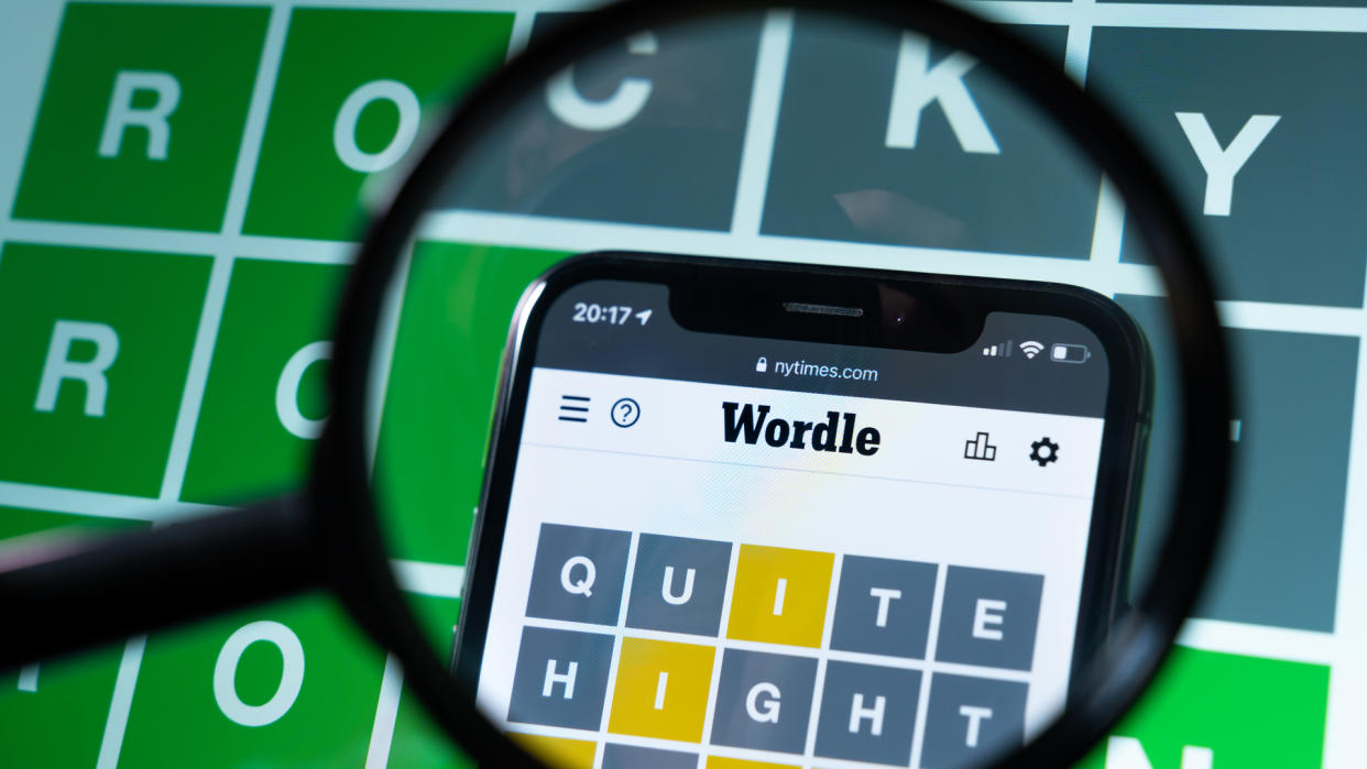  Wordle game through a magnifying glass. Daily WORDLE puzzle on a smartphone and on computer display. 