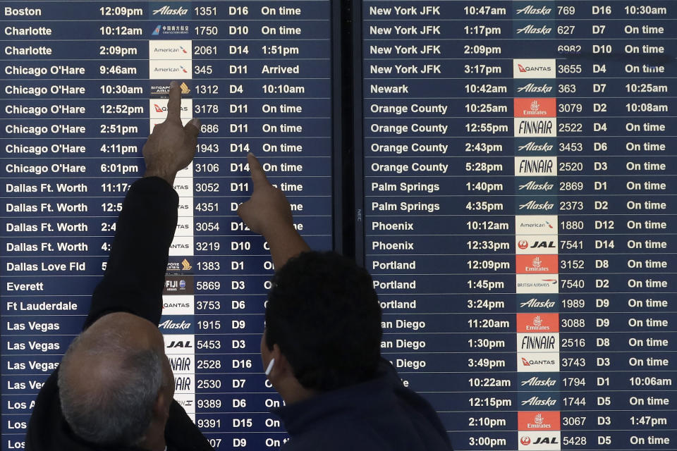 Two men point toward plane arrivals on a flight information board at San Francisco International Airport in San Francisco, Tuesday, Nov. 26, 2019. Northern California and southern Oregon residents are bracing for a 'bomb cyclone' that's expected at one of the busiest travel times of the year. (AP Photo/Jeff Chiu)