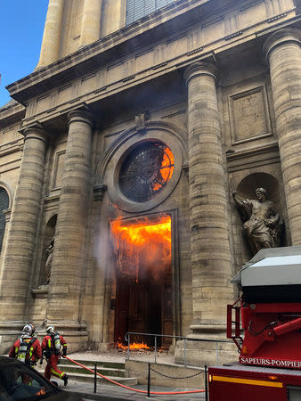 Members of the fire brigade run as a Saint-Sulpice church is seen on fire in Paris, France, March 17, 2019 in this still image taken from social media obtained on March 18, 2019. INSTAGRAM @agneswebste/via REUTERS