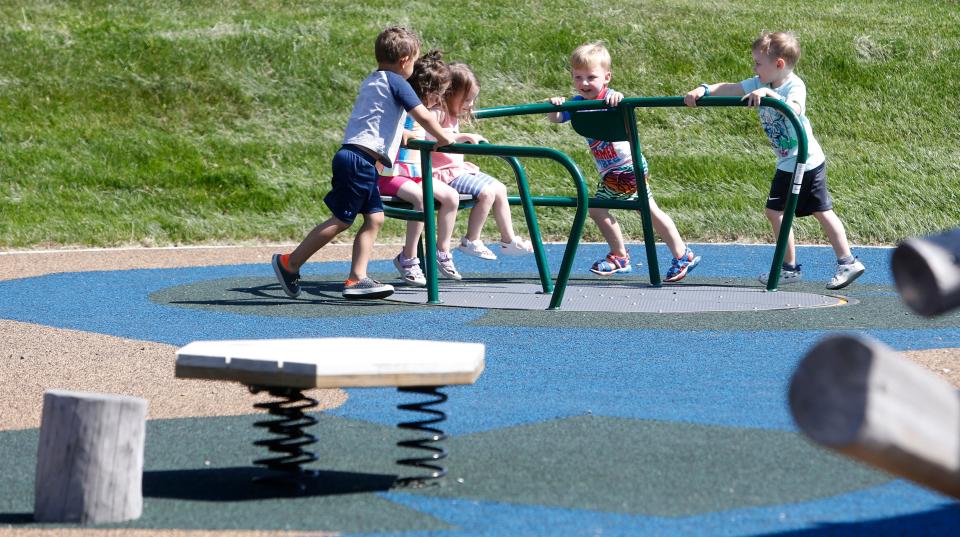 Children play on a merry-go-round Thursday, May 23, 2024, during the dedication and ribbon-cutting ceremony for the newly renovated Crawford Park in Mishawaka.