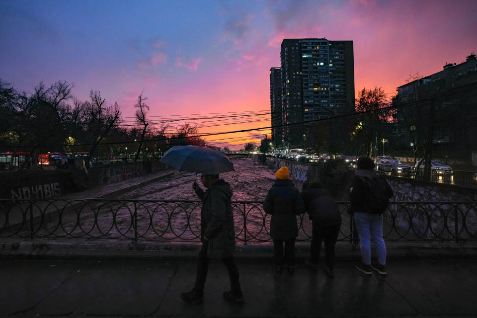 People watch the water level of the Mapocho River rise during a heavy rainfall, in downtown Santiago, Chile, Friday, June 23, 2023. (AP Photo/Esteban Felix)
