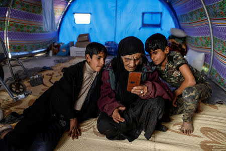 Khatla Ali Abdullah , 90, who recently fled her house in Al Mamoun district looks at photographs on a mobile phone as she sits with her grandsons in her tent in Hammam al Alil camp while Iraqi forces battle with Islamic State militants, in western Mosul, Iraq March 1, 2017. REUTERS/Zohra Bensemra