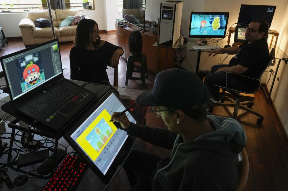 Adrián Díaz, centro, Ginette Hernández, izquierda, y Leonardo Gimón, derecha, trabajan en la creación del primer capítulo de una serie infantil animada llamada Kam-Bur, en un departamento en Caracas, Venezuela, el viernes 1 de julio de 2022. El serie protagonizada por una heroína femenina con rasgos andróginos es dirigida a niños de entre 7 y 12 años en un país donde la creación de este tipo de dibujos es casi nula. (Foto AP/Ariana Cubillos)