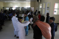 FILE - In this March 18, 2020 file photo, Afghan health workers measure the temperature of Afghan refugees to screen for coronavirus as they enter Afghanistan at the Islam Qala border crossing with Iran, in the western Herat Province. Some 200,000 Afghans and counting have returned from Iran to their home country after losing their jobs in the coronavirus pandemic or out of fear of getting infected. They are flowing across the border from a country that has one of the world's worst outbreak to an impoverished nation that is woefully unprepared to deal with the virus. (AP Photo/Hamed Sarfarazi, File)