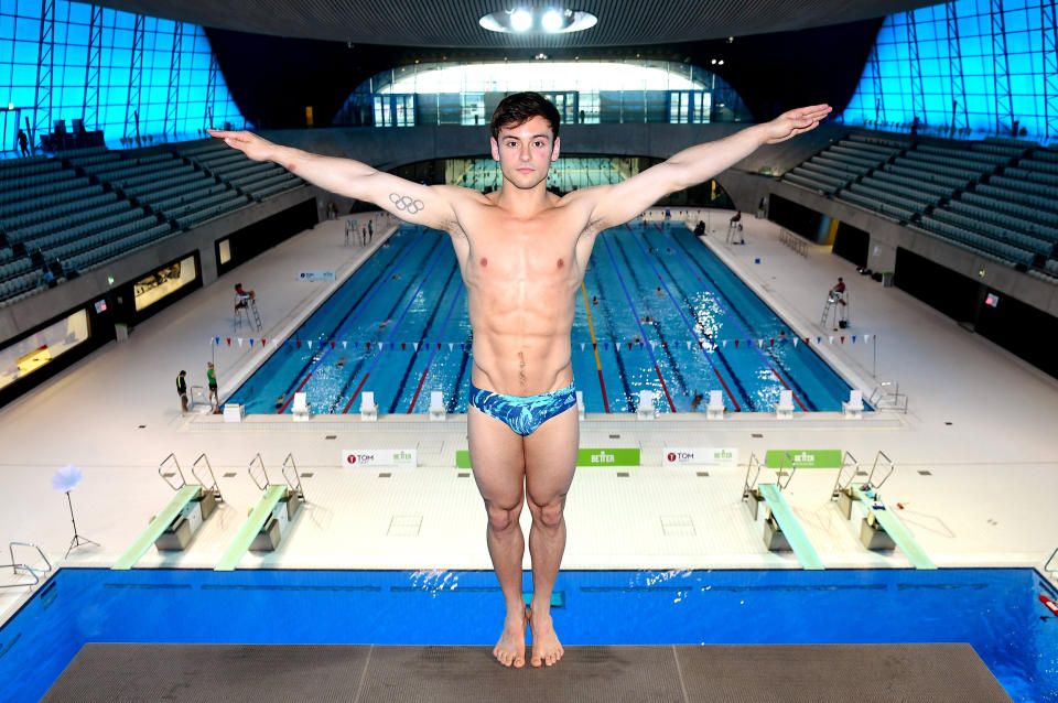 Tom Daley stands on the diving platform with his back to the water and both hands raised to his sides (Ian West / AP)