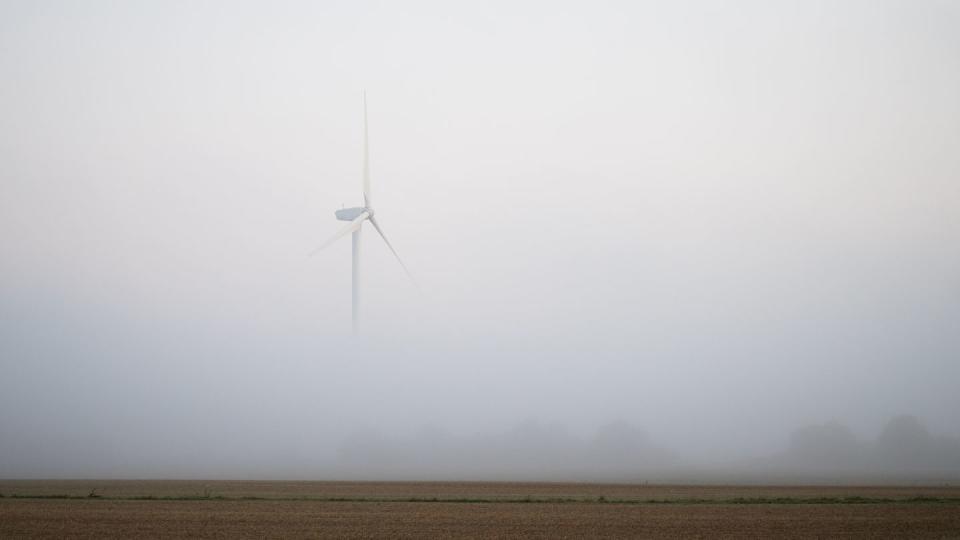 Ein Windrad ragt bei Hannover aus dem morgendlichen Nebel.