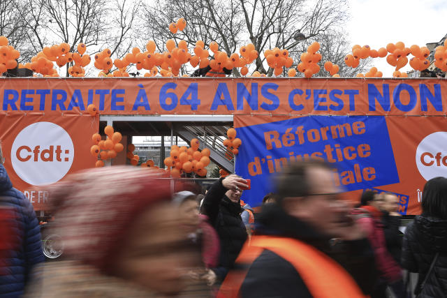 Demonstrators walk past an union banner opposing to retirement at age 64 during a demonstration, Tuesday, March 7, 2023 in Paris. Garbage collectors, utility workers and train drivers are among people walking off the job across France to show their anger at a bill raising the retirement age to 64, which unions see as a broader threat to the French social model. (AP Photo/Aurelien Morissard)