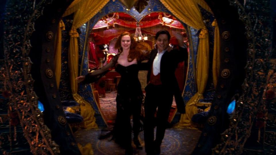 Nicole Kidman and Ewan McGregor step out from a large window and into the night in a scene from Moulin Rouge!