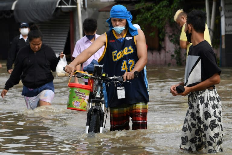 Des habitants portent leurs vélos dans une rue inondée  de la ville de Kawit, le 30 octobre 2022 (AFP - Ted ALJIBE)