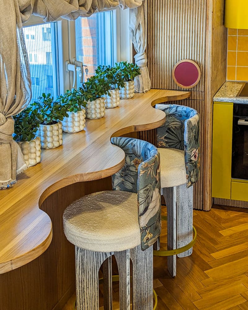 wavy wood window counter with botanical fabric backed stools and lots of potted plants