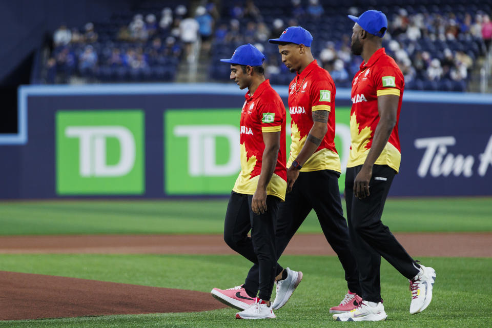 Canadian cricket team captain Saad Bin Zafar leads teammates Nicholas Kirton, middle, and Jeremy Gordon, right, to the mound ahead of throwing out the ceremonial first pitch at the Toronto Blue Jays' baseeball game against the Minnesota Twins in Toronto on Friday, May 10, 2024. (Cole Burston/The Canadian Press via AP)