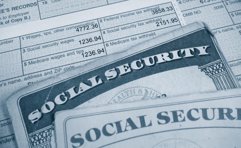 Two Social Security cards lying atop a W2 tax form that's highlighting payroll taxes paid.