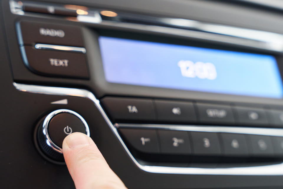 Finger pressing the power button on a car stereo system