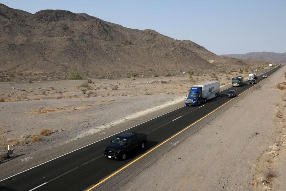 Cars and big rigs motor along a desert highway.