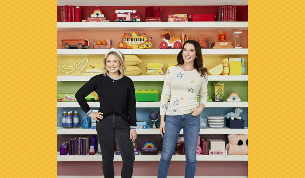 Joanna and Clea standing in front of a rainbow wall of shelves