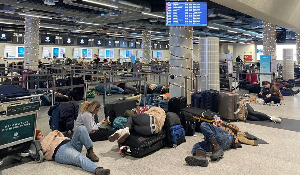 photo of stranded travelers sleeping on the ground, on top of luggage, and on the baggage claim conveyor.