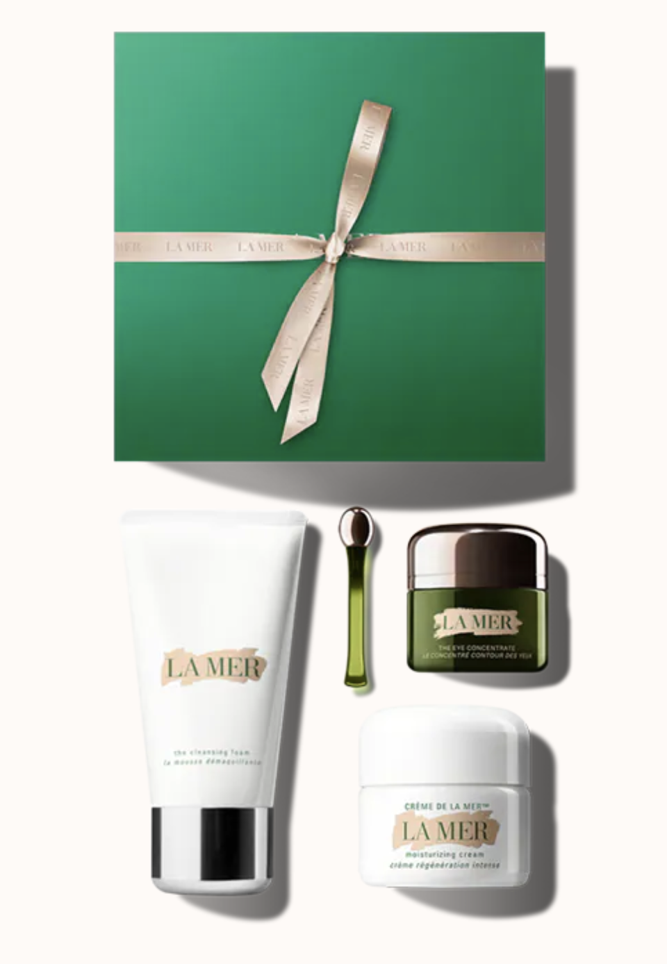 La Mer's Ultimate Starter Set shown on a white background, including a green box tied with ribbon, a white tube, a green applicator and two tubs, one white, one green.