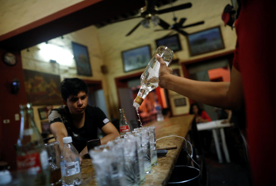 A resident watches as the bartender pours tequila for a traditional drink called a 