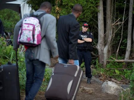 A Royal Canadian Mounted Police (RCMP) officer watches as two men who stated they are from Haiti cross the US-Canada border into Canada from Roxham Road in Champlain, New York, U.S. August 11, 2017. REUTERS/Christinne Muschi