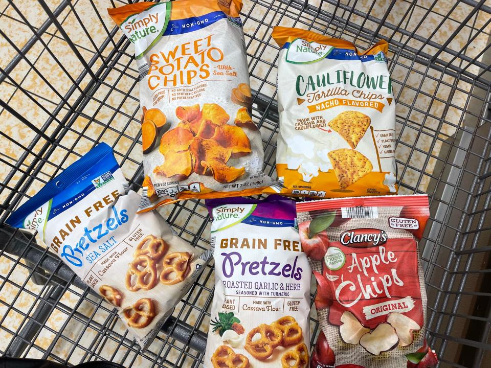 Five bags of chips in a cart: Simply Nature grain-free pretzels with sea salt, Simply Nature roasted-garlic-and-herb flavored grain-free pretzels, Simply Nature sweet-potato chips with sea salt, Simply Nature nacho-flavored cauliflower tortilla chips, and Clancy's apple chips.