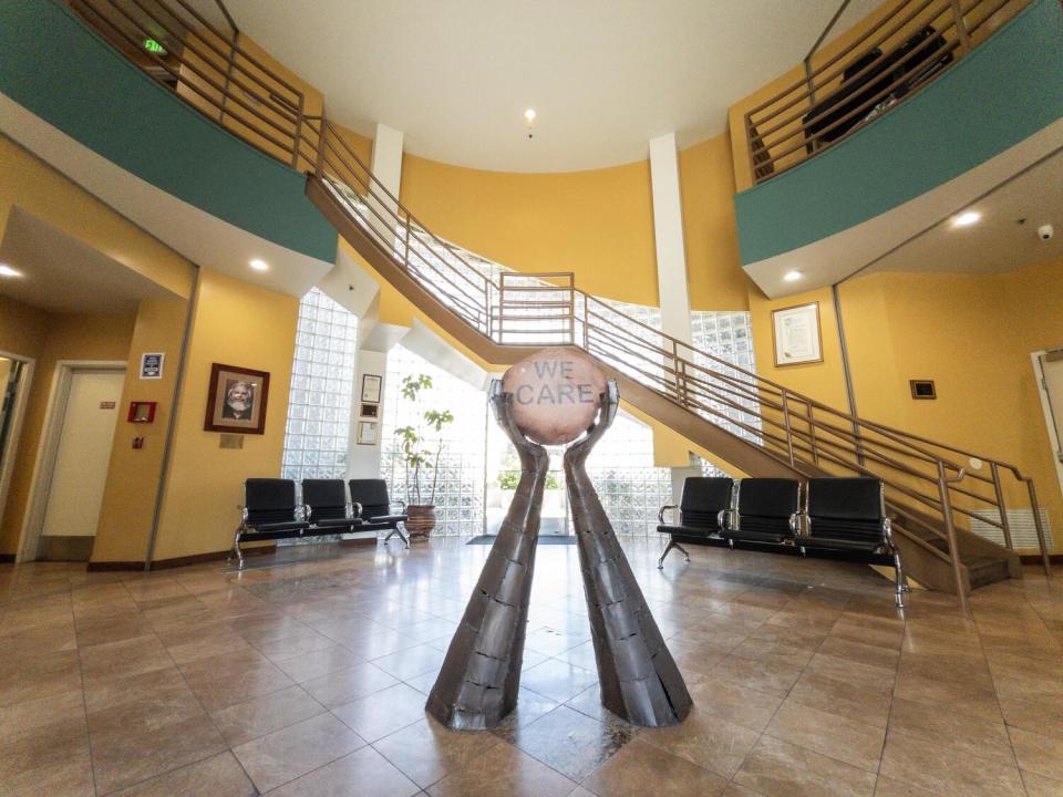 A building interior, with a staircase and chairs. In the center two hands hold up a sign reading "We care."