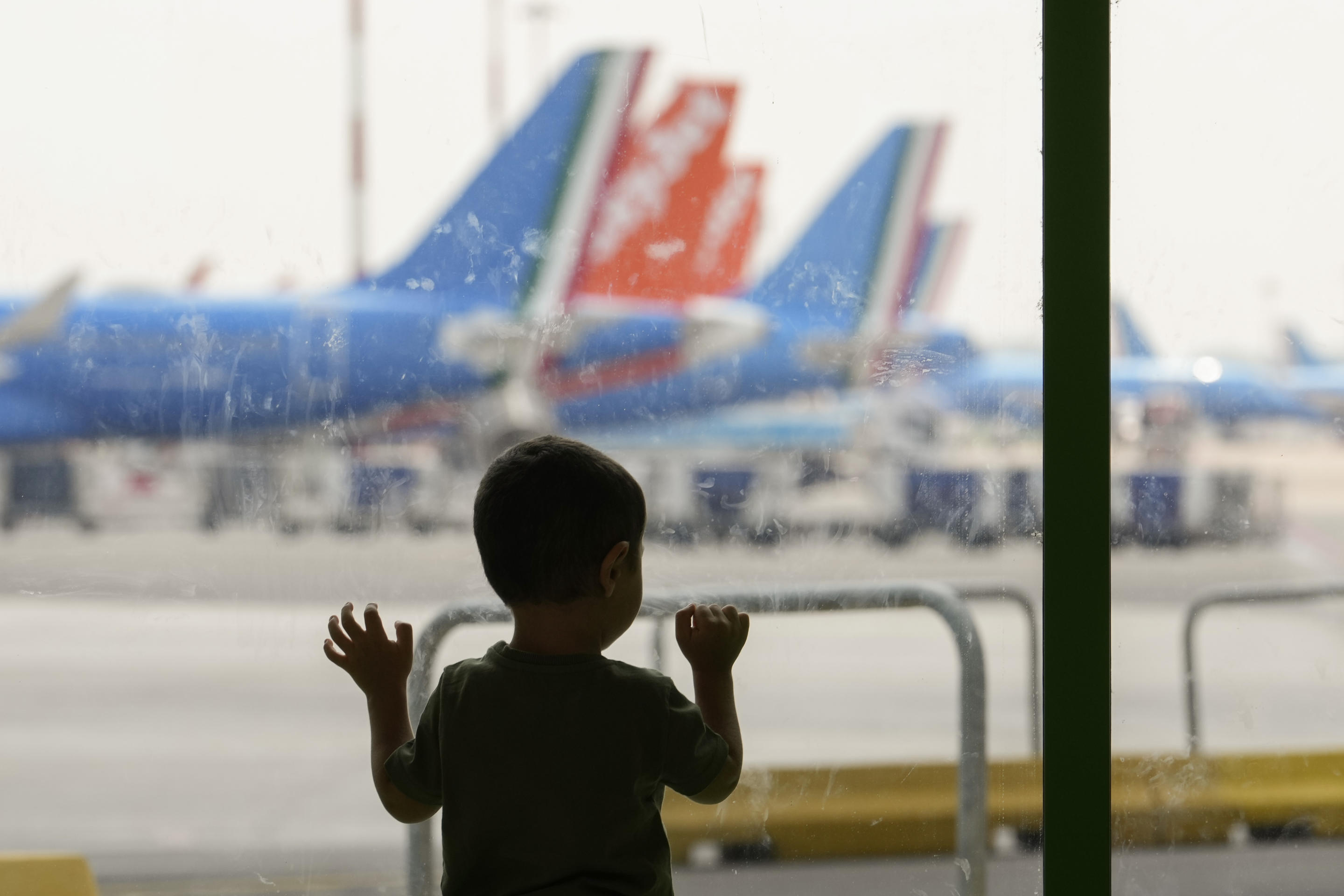 A child looks out the window at parked planes as he waits at Linate Airport in Milan.