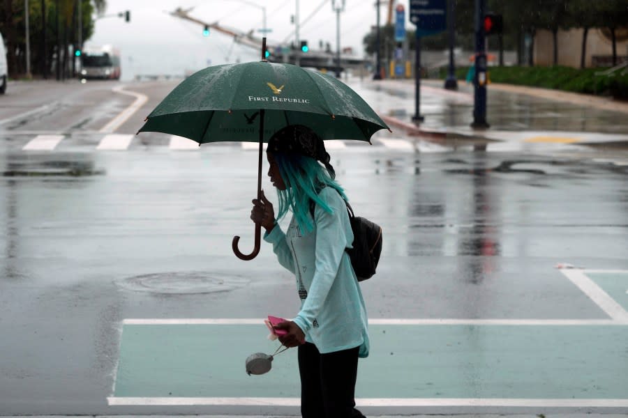 A pedestrian walks under a light rain by the Waterfront Park in downtown San Diego, Sunday, Aug. 20, 2023. Tropical Storm Hilary swirled northward Sunday just off the coast of Mexico's Baja California peninsula, no longer a hurricane but still carrying so much rain that forecasters said "catastrophic and life-threatening" flooding is likely across a broad region of the southwestern U.S. (AP Photo/Damian Dovarganes)