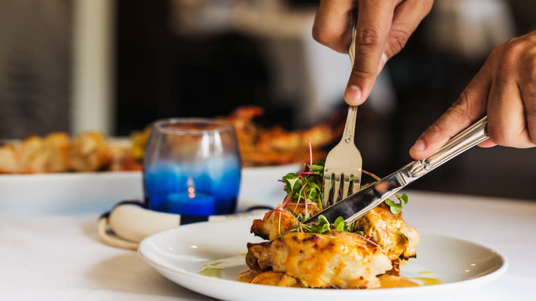 person cutting chicken with knife on white plate