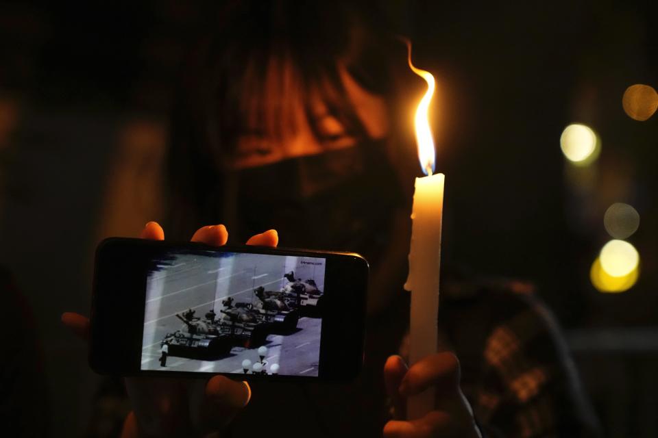 FILE - A woman holds up a ligt candle and a phone showing the image of the 1989 tank man protester during a candle vigil to mark the anniversary of the military crackdown on a pro-democracy student movement in Beijing, outside Victoria Park in Hong Kong, Friday, June 4, 2021. As Beijing prepares to hold the Winter Olympics opening in February 2022, China's president and party leader Xi Jinping appears firmly in control. The party has made political stability paramount and says that has been the foundation for the economic growth that has bettered lives and put the nation on a path to becoming a regional if not global power. (AP Photo/Kin Cheung, File)