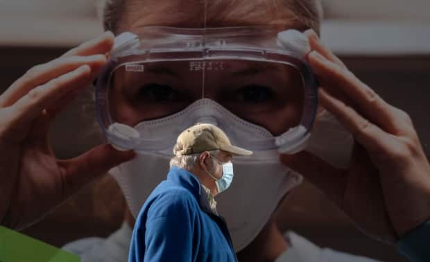 A man wears a protective face mask to help prevent the spread of COVID-19 as he walks past a billboard in Vancouver. 