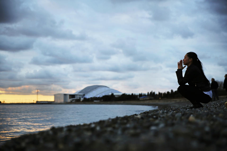 Elina Suyundikova, a dancer in the 2014 Winter Olympics opening ceremony, watches the sunset along the Black Sea while returning from a rehearsal on the eve of the performance and the games' official opening at Fisht Olympic Stadium, seen in the background, Thursday, Feb. 6, 2014, in Sochi, Russia. (AP Photo/David Goldman)