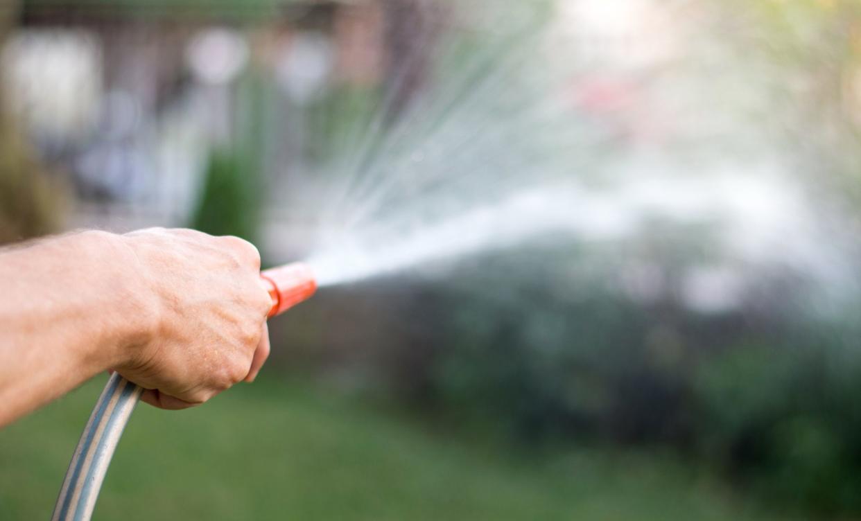 Man watering flowers with a hose outside