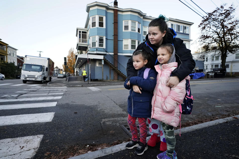 Adrienne Dyment holds her daughters Sophia, left, and Paizley, while waiting for the school bus to arrive as school resumes in the wake of last week's mass shootings, Tuesday, Oct. 31, 2023, in Lewiston, Maine. (AP Photo/Robert F. Bukaty)