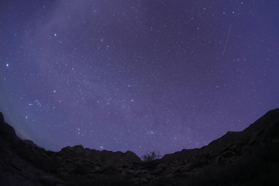 a meteor streaks through a starry sky above mountains