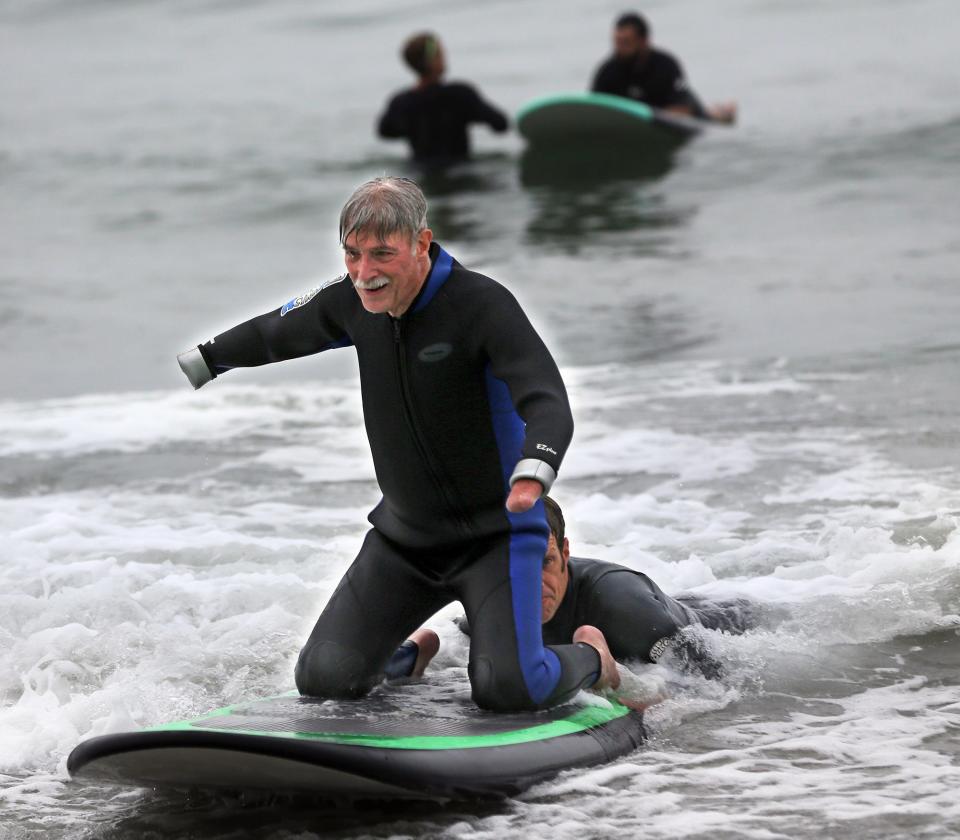 The Wounded Warrior Project returned to Hampton’s North Beach for its 14th Hit The Beach Friday, Aug. 26, 2022. Veteran Jerry Miserandino balances on his knees while experiencing the waves bringing him in with a little help from another surfer.