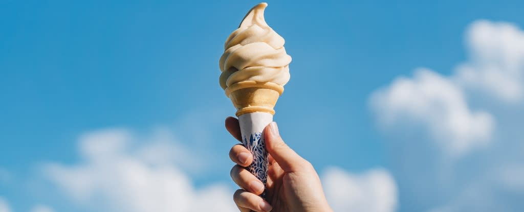 A hand holding an ice cream with a blue sky in the background