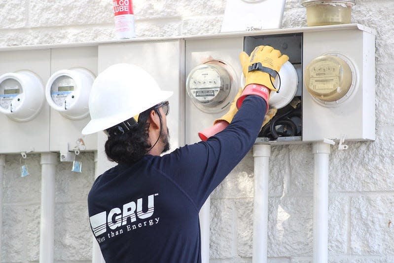 An employee for Gainesvilel Regional Utilities installs an AMI (Advanced Metering Infrastructure) device on the side of a building.