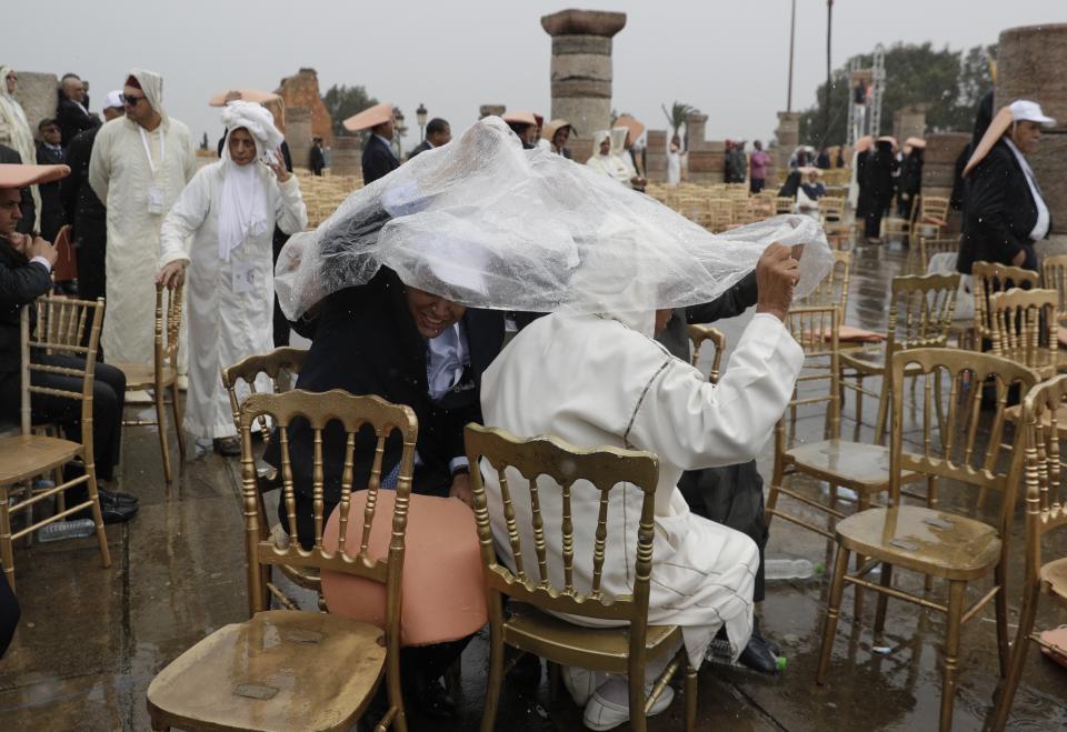 People shelter from the rain as they wait for Pope Francis to deliver his speech in Rabat, Morocco, Saturday, March 30, 2019. Francis's weekend trip to Morocco aims to highlight the North African nation's tradition of Christian-Muslim ties while also letting him show solidarity with migrants at Europe's door and tend to a tiny Catholic flock on the peripheries. (AP Photo/Gregorio Borgia)