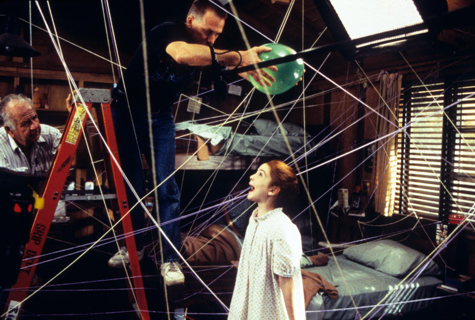 Dana Carvey and young Juliette Brewer in a behind-the-scenes moment from the film "Clean Slate," with a crew member adjusting a green balloon in a web of strings