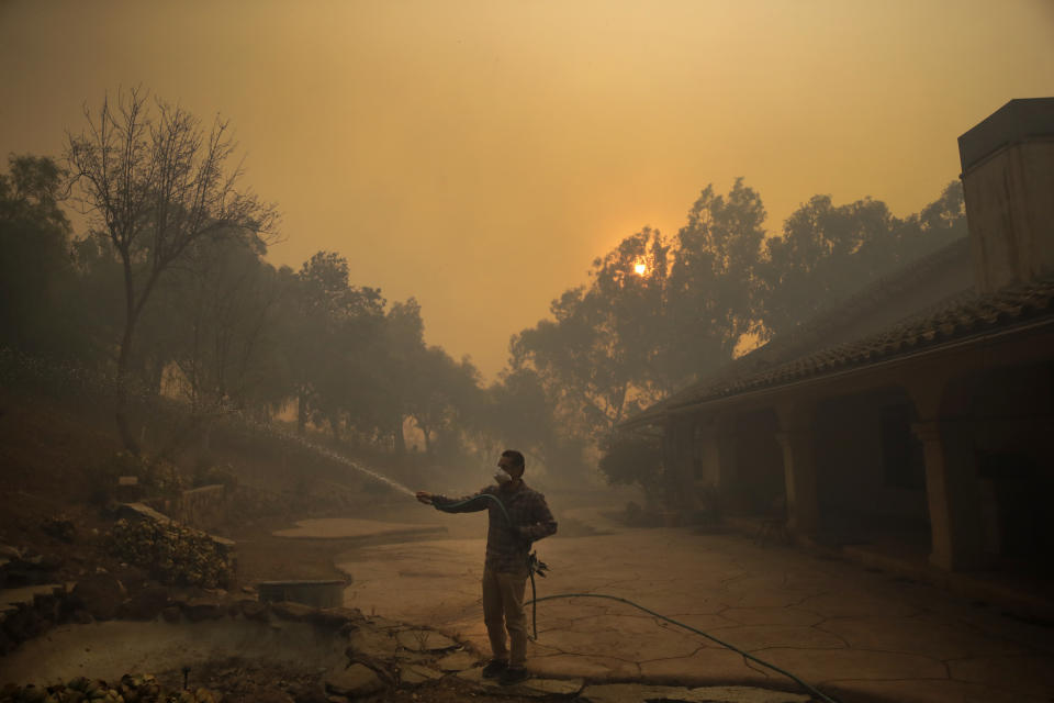 Marco Alcaraz uses a garden hose to protect his girlfriend's home as the Easy fire approaches Wednesday, Oct. 30, 2019, in Simi Valley, Calif. A new wildfire erupted Wednesday in wind-whipped Southern California, forcing the evacuation of the Ronald Reagan Presidential Library and nearby homes, as both ends of the state struggled with blazes, dangerously gusty weather and deliberate blackouts. (AP Photo/Marcio Jose Sanchez)