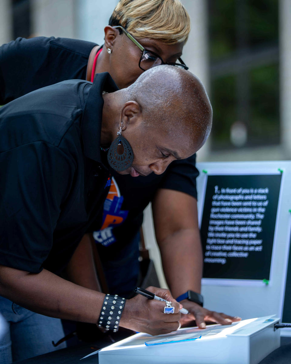 Wanda Ridgeway (above) watches as Retha Rogers (below) traces a photograph at an event honoring victims of gun violence as part of public artwork project in Rochester, N.Y. on Aug. 4, 2023. The event was a collaboration between artists Martin Krafft and Elena Makansi and Rise Up Rochester, held at the Rochester Contemporary Art Center.