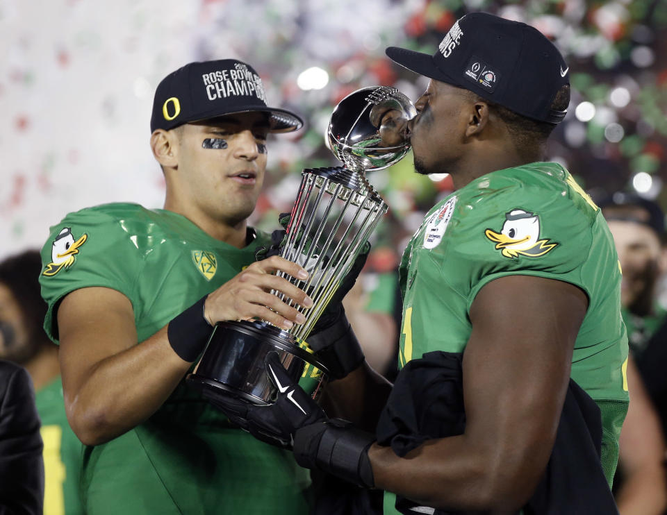 Oregon quarterback Marcus Mariota, left, and linebacker Tony Washington celebrate with the trophy after their win against Florida State during the second half of the Rose Bowl NCAA college football playoff semifinal, Thursday, Jan. 1, 2015, in Pasadena, Calif. (AP Photo/Lenny Ignelzi)