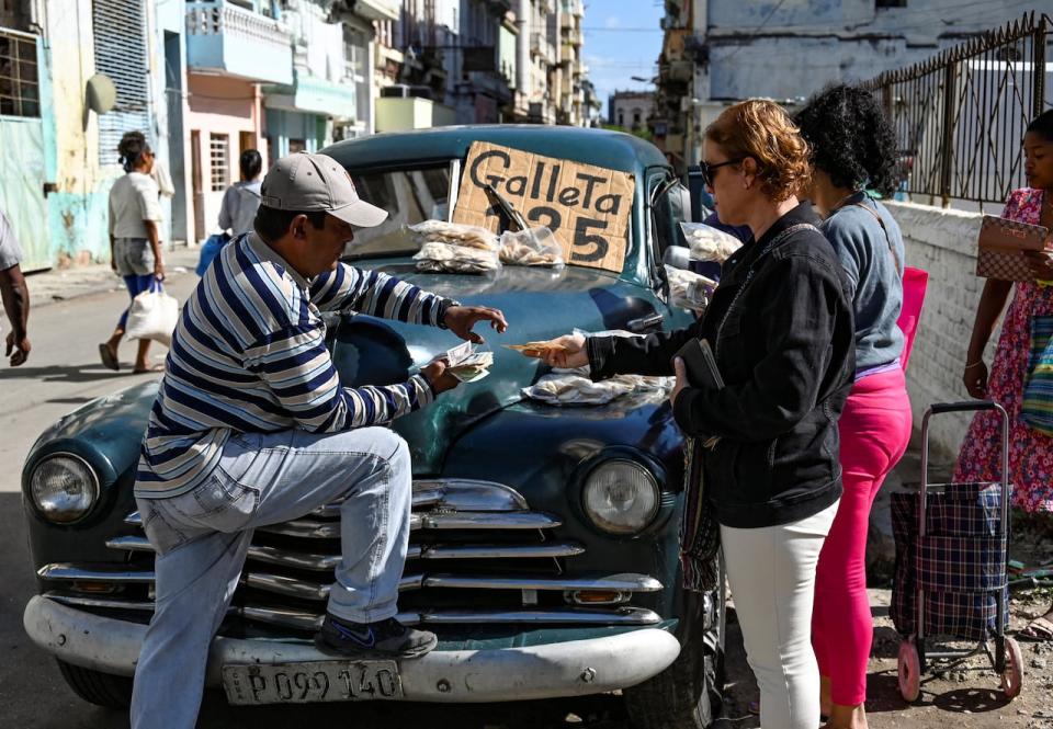 A man sells cookies on an old American car in Havana on December 20, 2023. Cuba's economy will shrink by up to 2% this year, Finance Minister Alejandro Gil estimated on Wednesday, after acknowledging that the country will not be able to achieve the projected economic growth of 3% by 2023. 