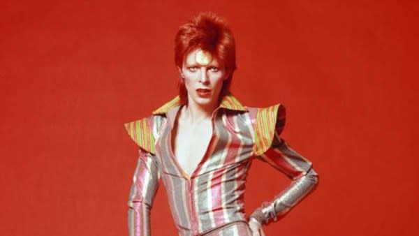 A queer Halloween costume for 2023. The image shows David Bowie from the waist up with bright red hair and a tight striped jumpsuit.