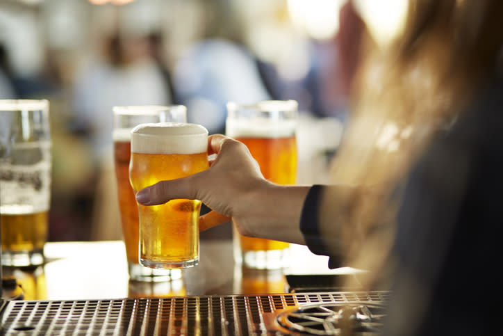 Person holding a glass of beer at a bar with other patrons and drinks in the background