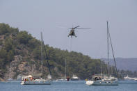 A helicopter takes water to pour on a wildfire that burns the forest in Turgut village, near tourist resort of Marmaris, Mugla, Turkey, Wednesday, Aug. 4, 2021. As Turkish fire crews pressed ahead Tuesday with their weeklong battle against blazes tearing through forests and villages on the country's southern coast, President Recep Tayyip Erdogan's government faced increased criticism over its apparent poor response and inadequate preparedness for large-scale wildfires.(AP Photo/Emre Tazegul)