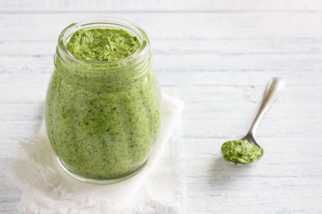 Fresh homemade pesto sauce from arugula with pine nuts in a glass jar on a blue wooden background